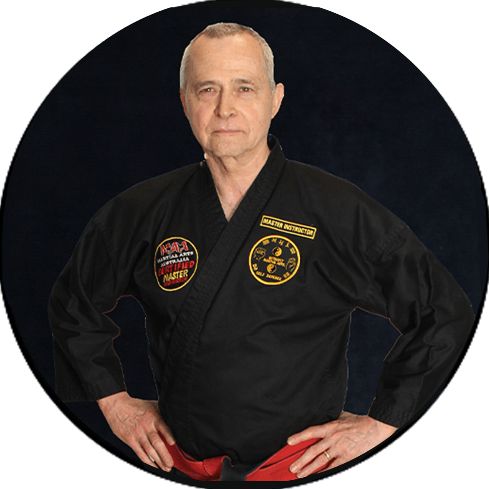 Man in black martial arts uniform with red belt, standing hands on hips against a dark background