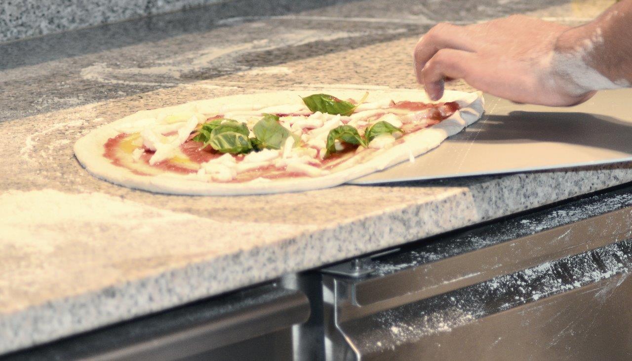 Pizza infornata. Mano che tiene la pizza su una pala e la trasferisce nel forno.