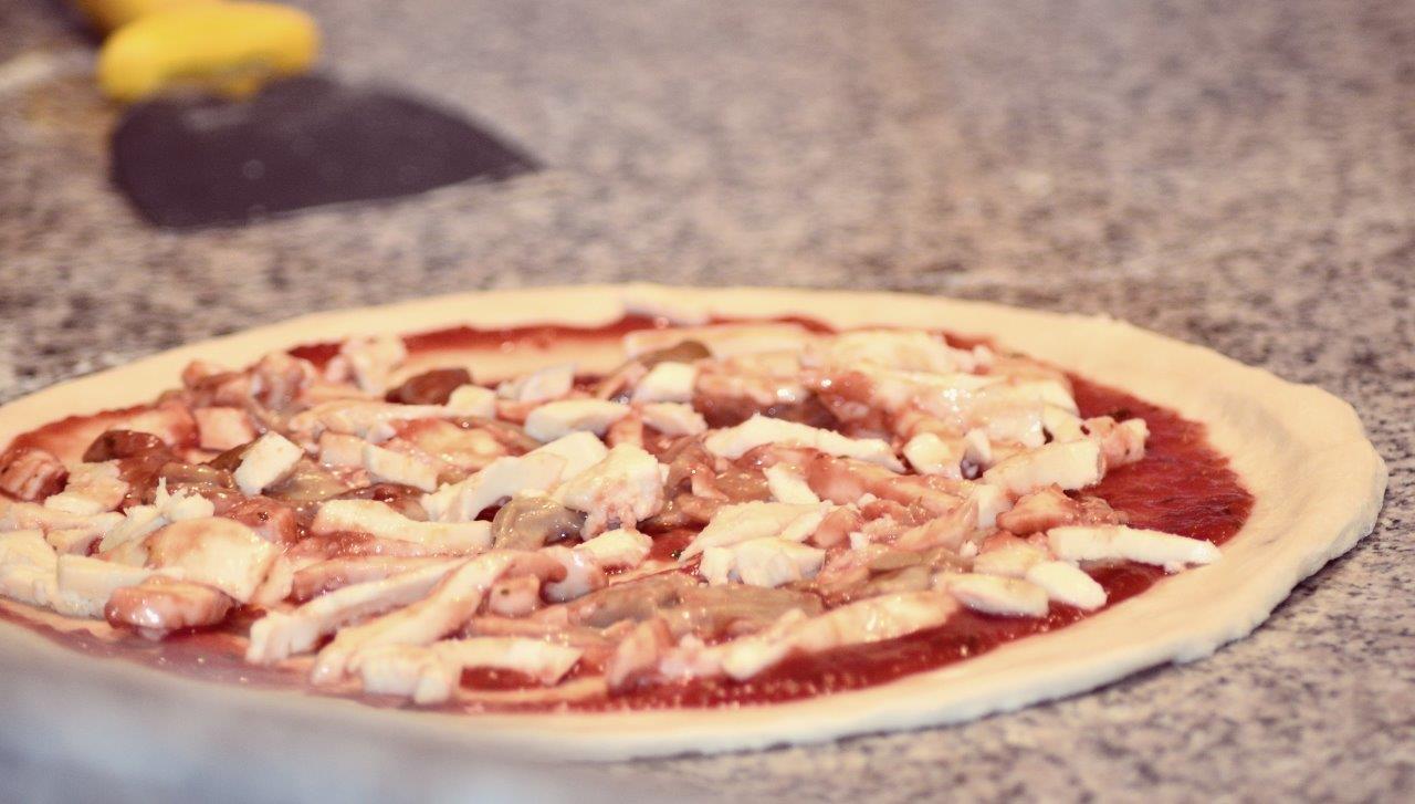 Impasto per pizza con salsa e condimenti su un piano di lavoro. Una pala per pizza si intravede sullo sfondo sfocato.