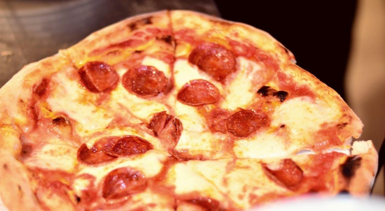 Pizza al pepperoni, parzialmente tagliata a fette, con mozzarella fusa e crosta dorata.