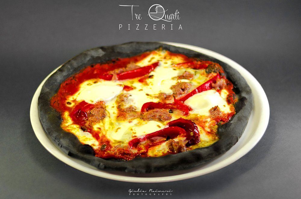 Pizza con crosta nera, salsa rossa, salsiccia, peperoni e mozzarella su un piatto bianco.