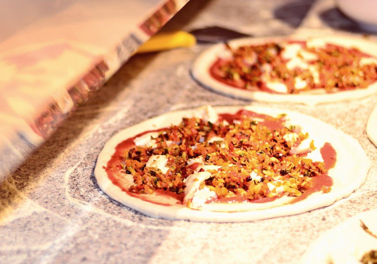 Due pizze condite su una superficie di marmo. Sullo sfondo una pala per pizza.