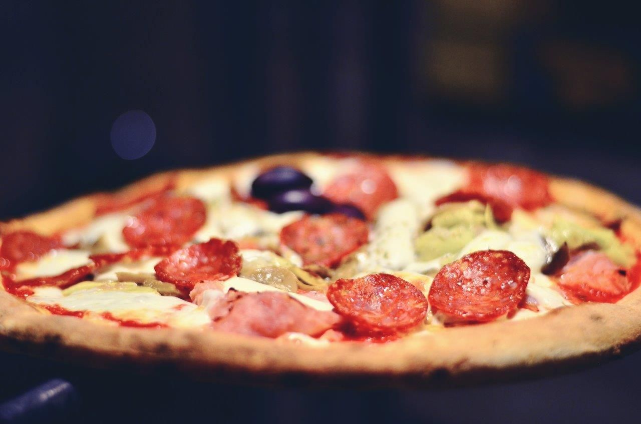 Pizza al pepperoni con formaggio, prosciutto, carciofi e cipolla, su uno sfondo scuro.