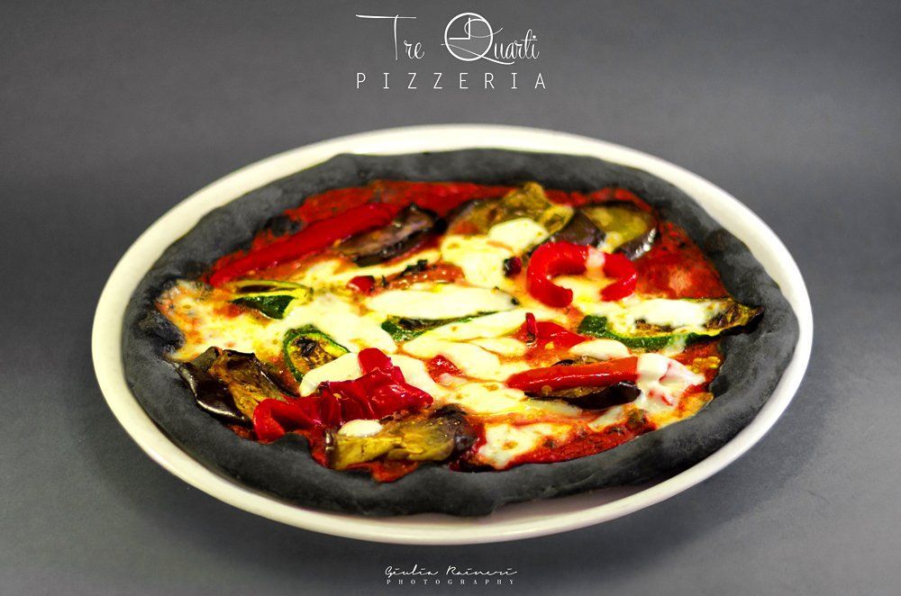 Pizza con crosta nera, farcita con verdure e formaggio, servita su un piatto bianco.