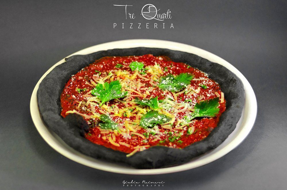 Pizza con crosta nera, salsa rossa, formaggio e prezzemolo su un piatto bianco.