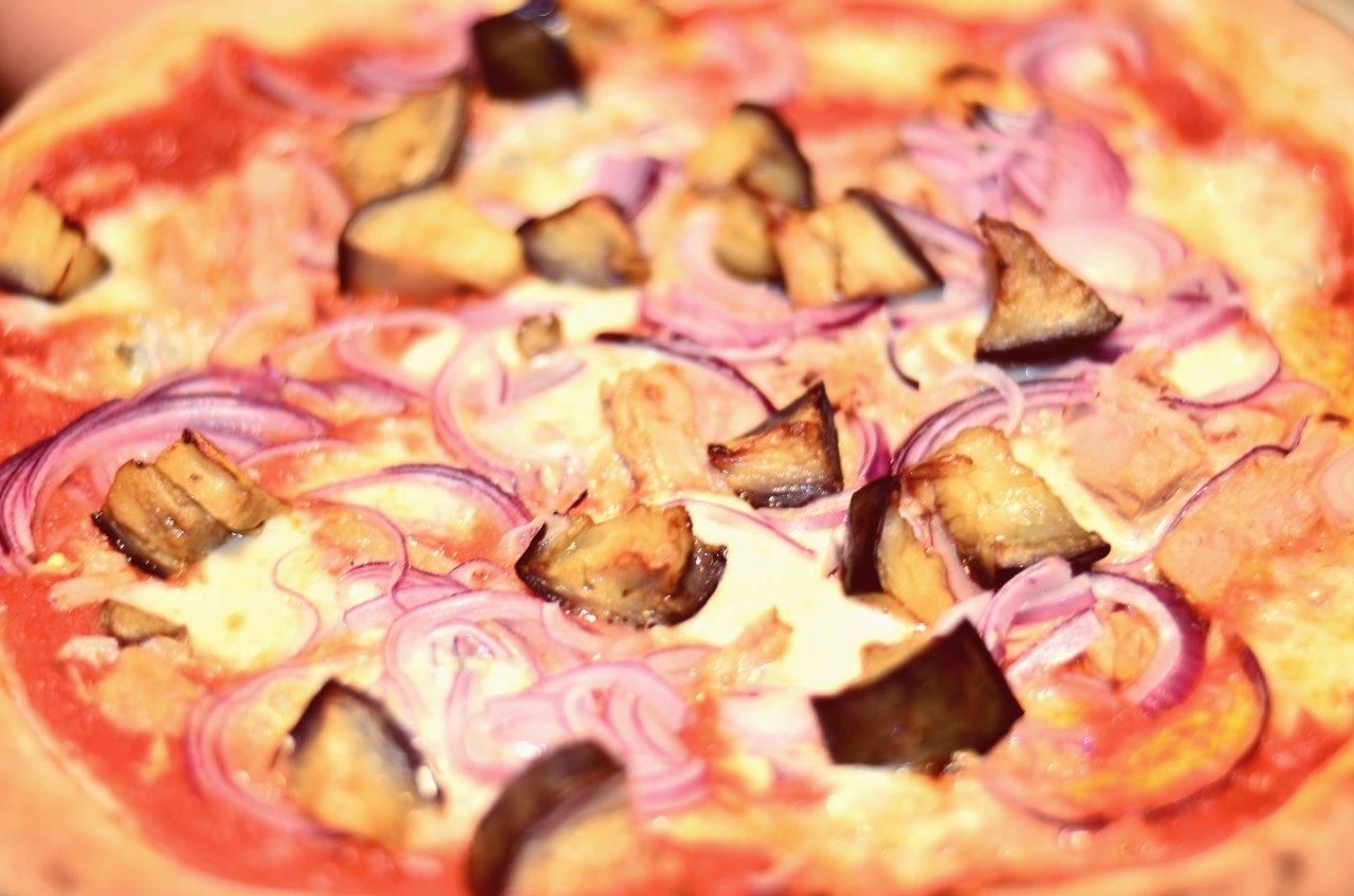 Pizza condita con cipolle rosse, melanzane e salsa.