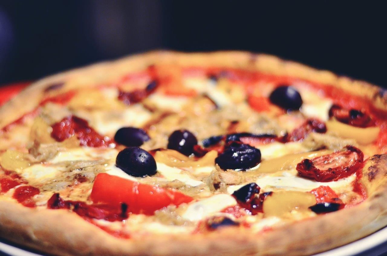 Pizza con salsa di pomodoro, olive e condimenti, primo piano, crosta dorata.