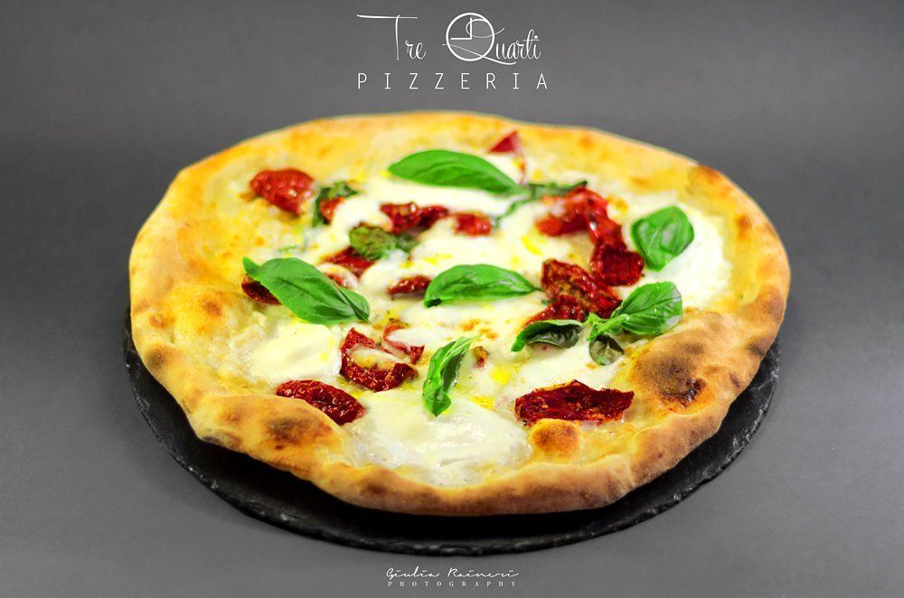 Pizza con mozzarella, pomodori secchi e basilico su un piatto scuro.