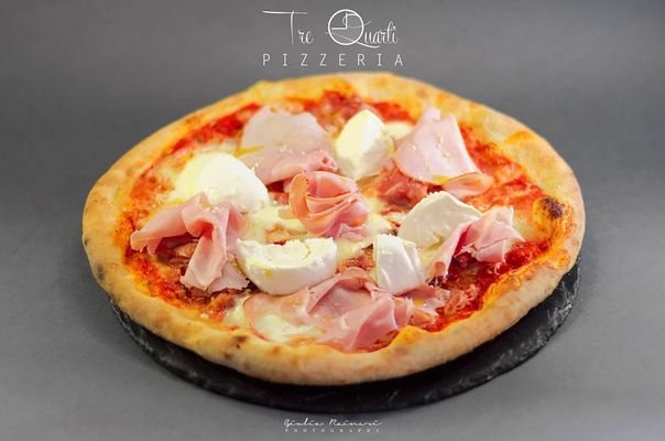 Pizza con prosciutto e mozzarella su una lavagna, su sfondo grigio.