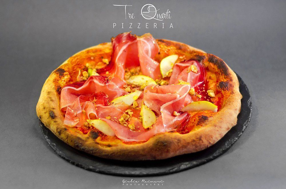Pizza con prosciutto, pere e noci su un piatto scuro.