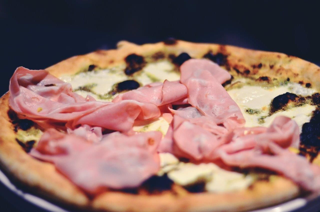 Pizza con prosciutto e formaggio su un piatto bianco; sfondo scuro.