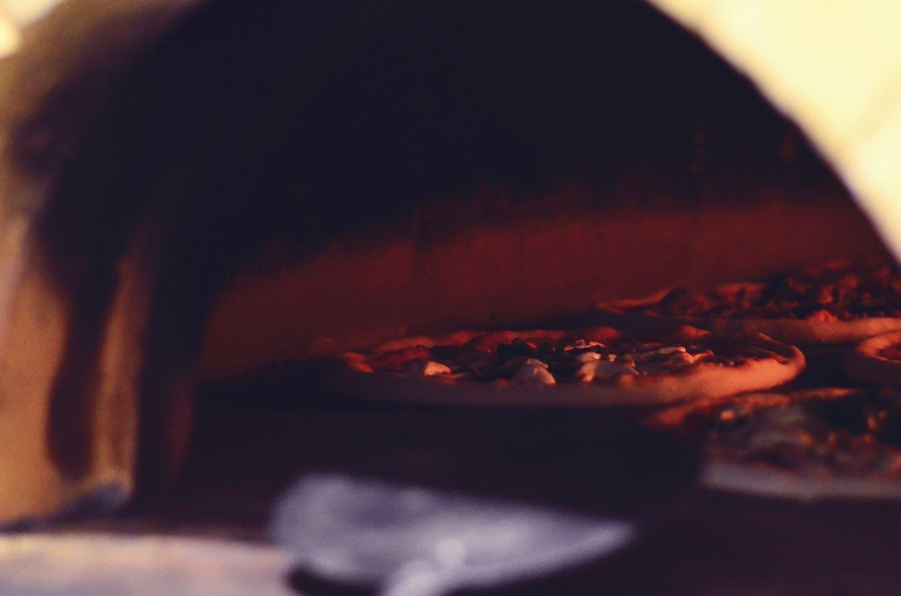 Pizza che cuoce in un forno a legna, con bagliore rosso visibile.
