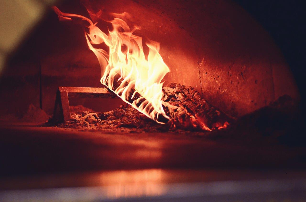 Fiamme che ardono in un forno per pizza in mattoni, illuminando l'interno con una luce arancione e rossa.