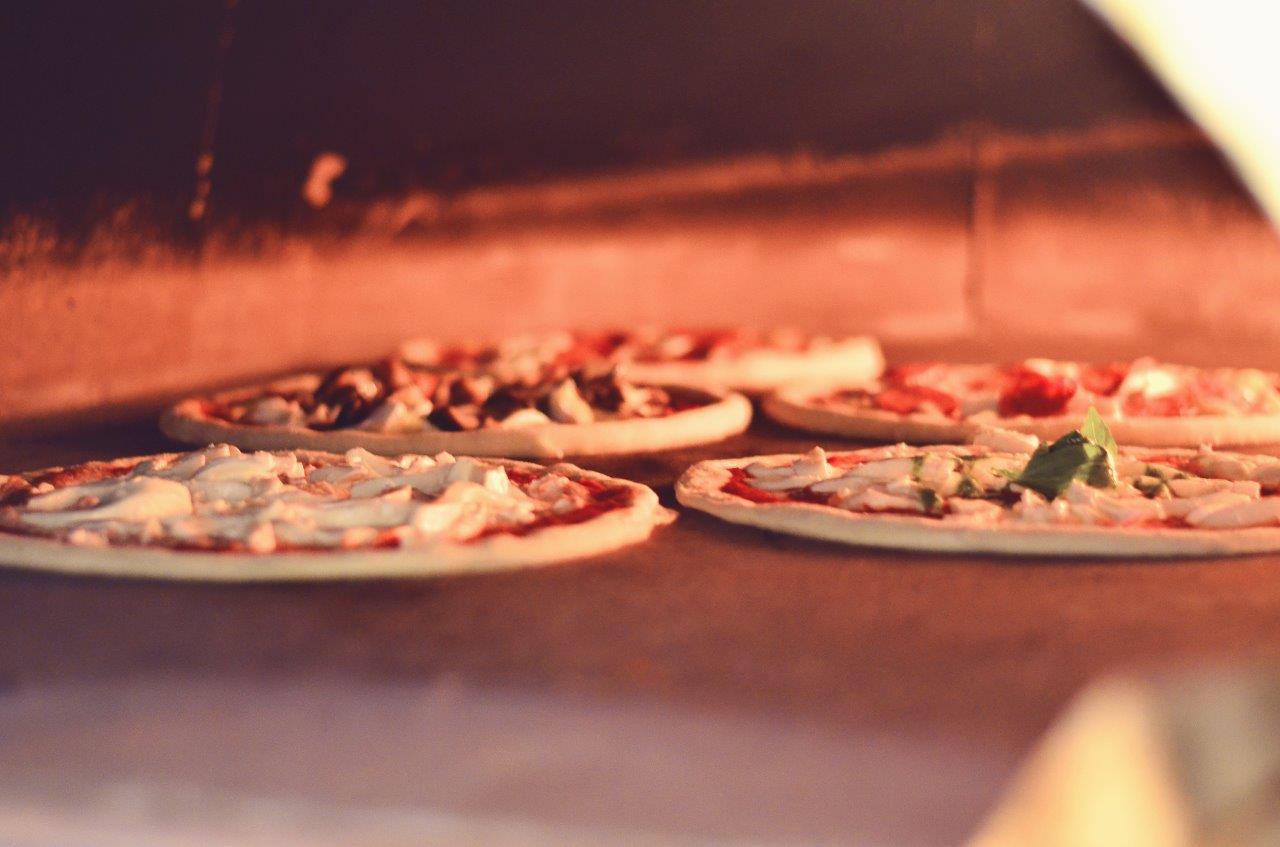 Quattro piccole pizze cotte in forno illuminato di rosso.