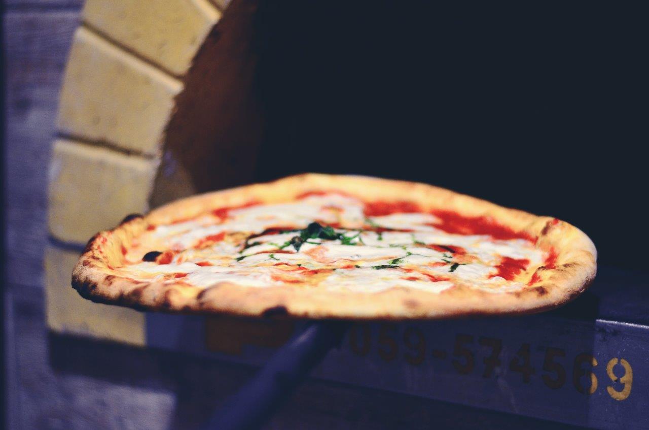 Pizza su pala appena tolta dal forno a legna; salsa rossa, formaggio bianco e basilico verde.