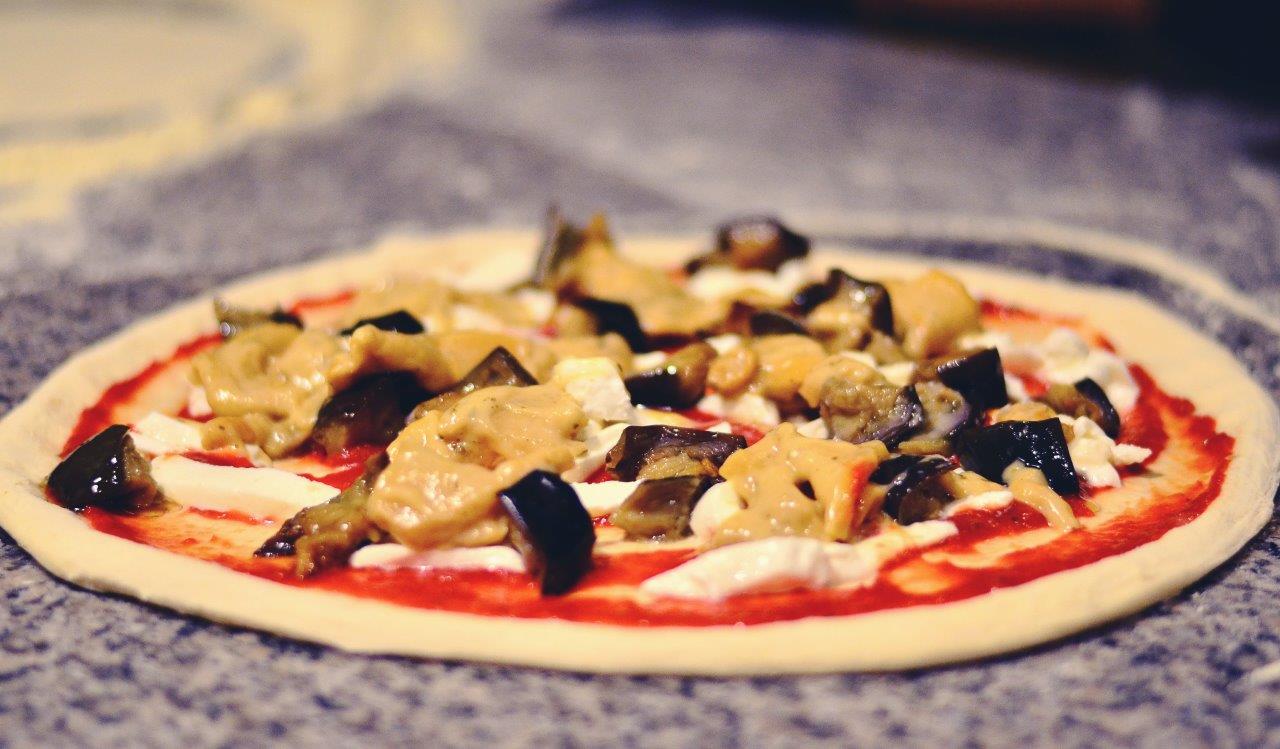 Pizza condita con salsa rossa, mozzarella e melanzane, pronta per essere infornata.