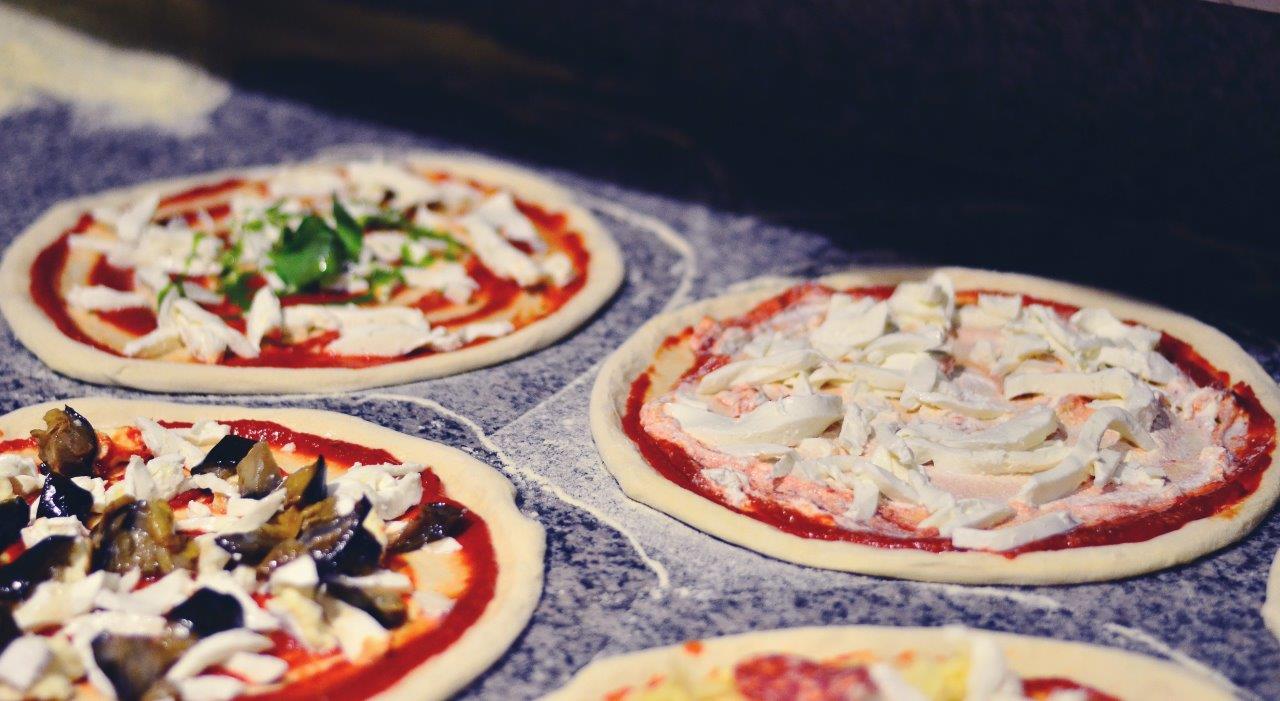 Quattro mini pizze farcite con salsa e vari ingredienti, disposte su una superficie in pietra.