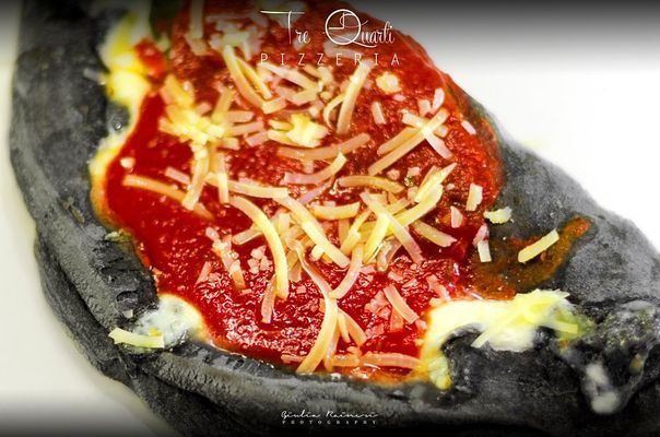 Base per pizza nera condita con salsa rossa, formaggio fuso e formaggio grattugiato.