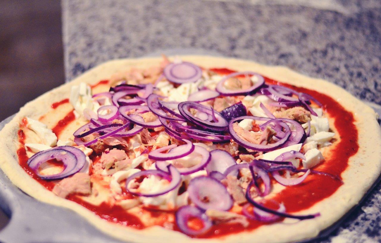 Pizza con salsa rossa, cipolla rossa e altri condimenti, cruda.