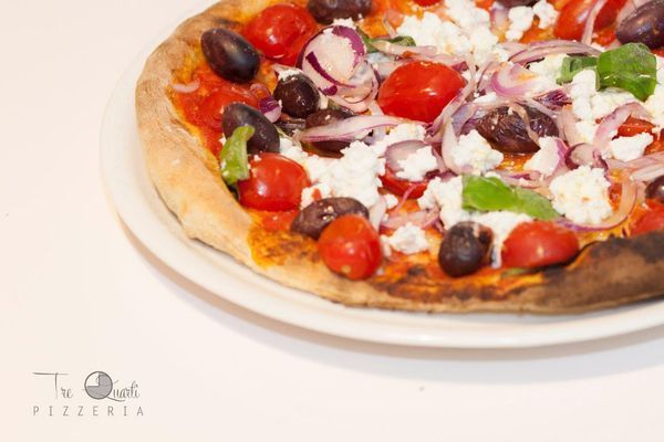 Pizza condita con salsa rossa, pomodori, olive, cipolla rossa e formaggio feta su un piatto bianco.