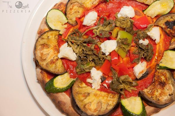 Pizza vegetariana con melanzane, zucchine, peperoni e formaggio, su un piatto bianco.