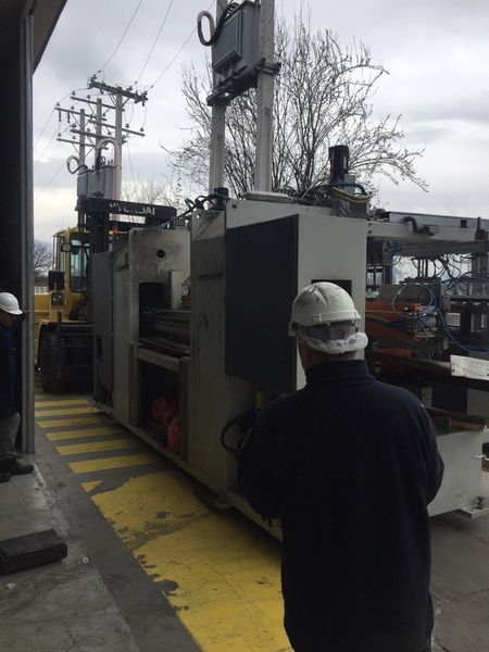 Obrero con casco de seguridad de pie junto a maquinaria industrial en una pasarela exterior mojada de una fábrica.