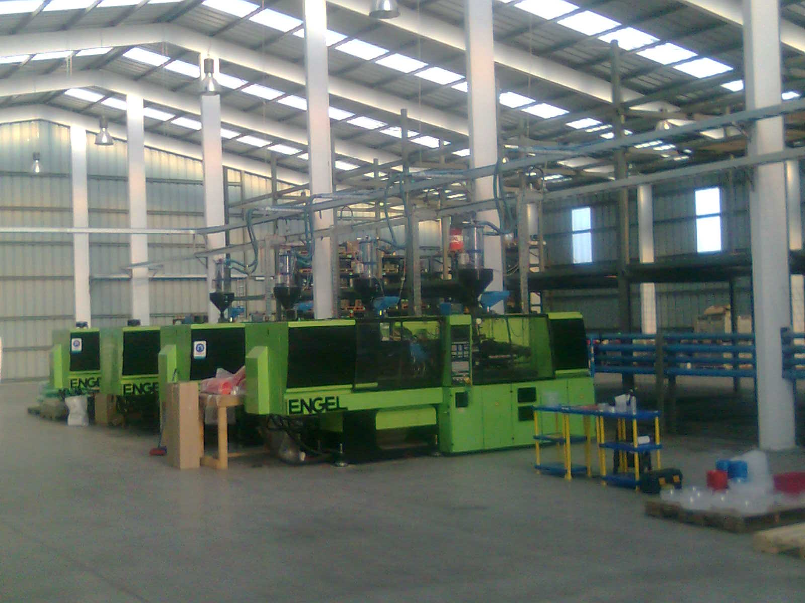 Máquina industrial verde en un gran taller de fábrica con techos altos y ventanas.