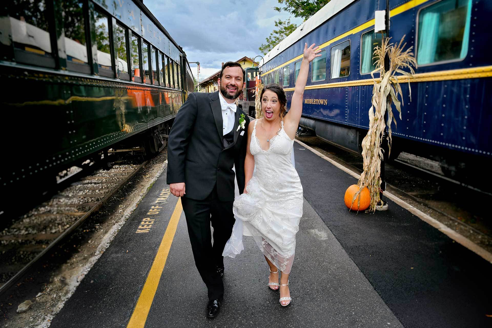 A bride and groom are walking in front of a train at Essex Steam Train wedding photographed by Rogers Photography in Connecticut. 
