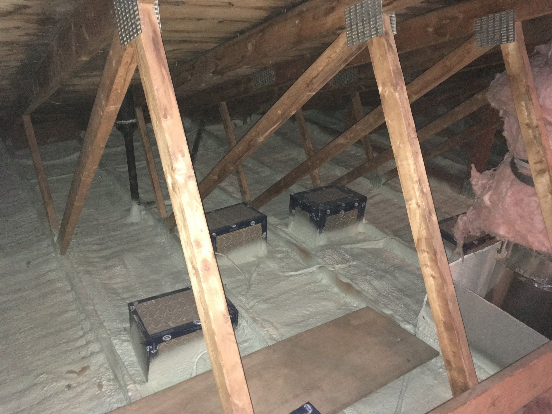An attic with wooden beams and insulation on the floor.