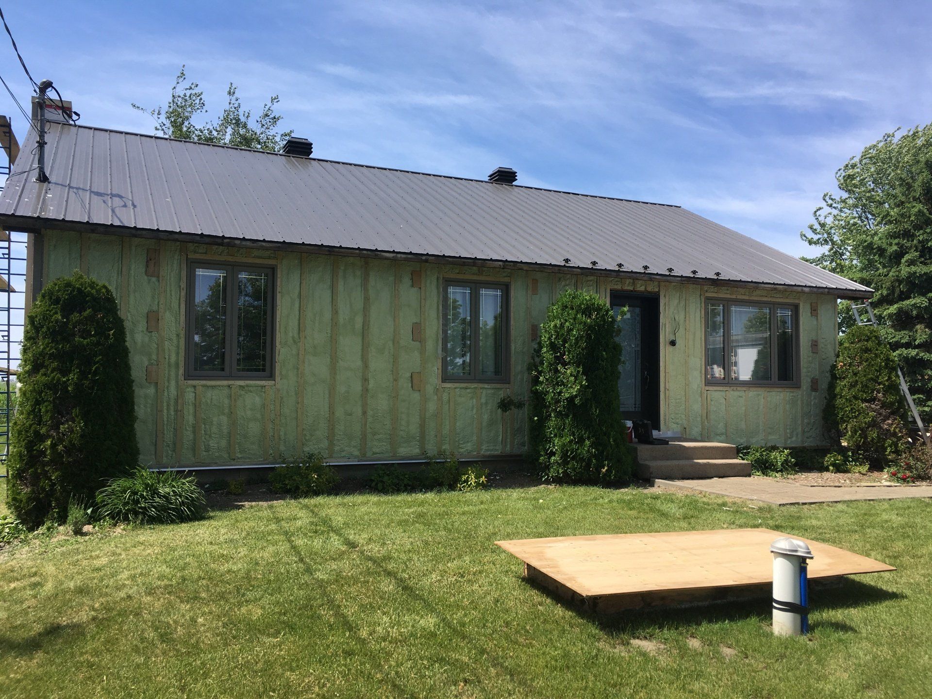 A house with a metal roof is sitting in the middle of a lush green field.