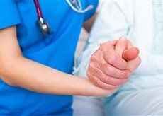 Krankenschwester im blauen Kittel hält die Hand eines älteren Patienten.