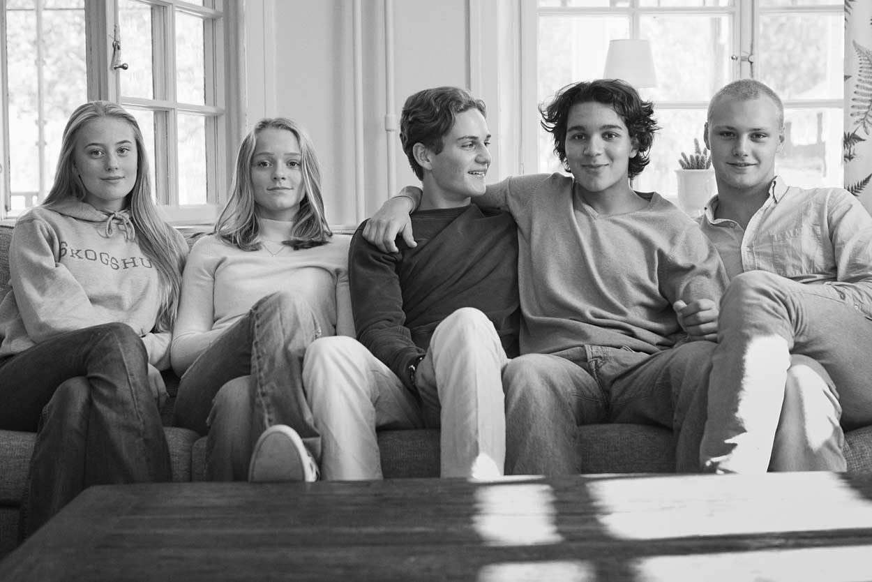 En grupp ungdomar sitter i en soffa i ett vardagsrum.