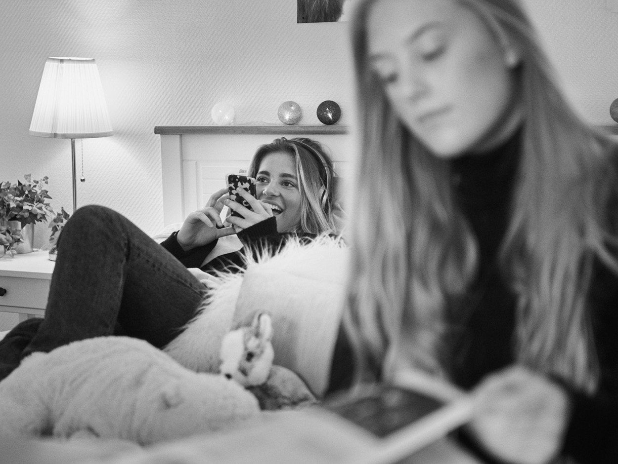 Två kvinnor sitter i en soffa och tittar på sina telefoner.