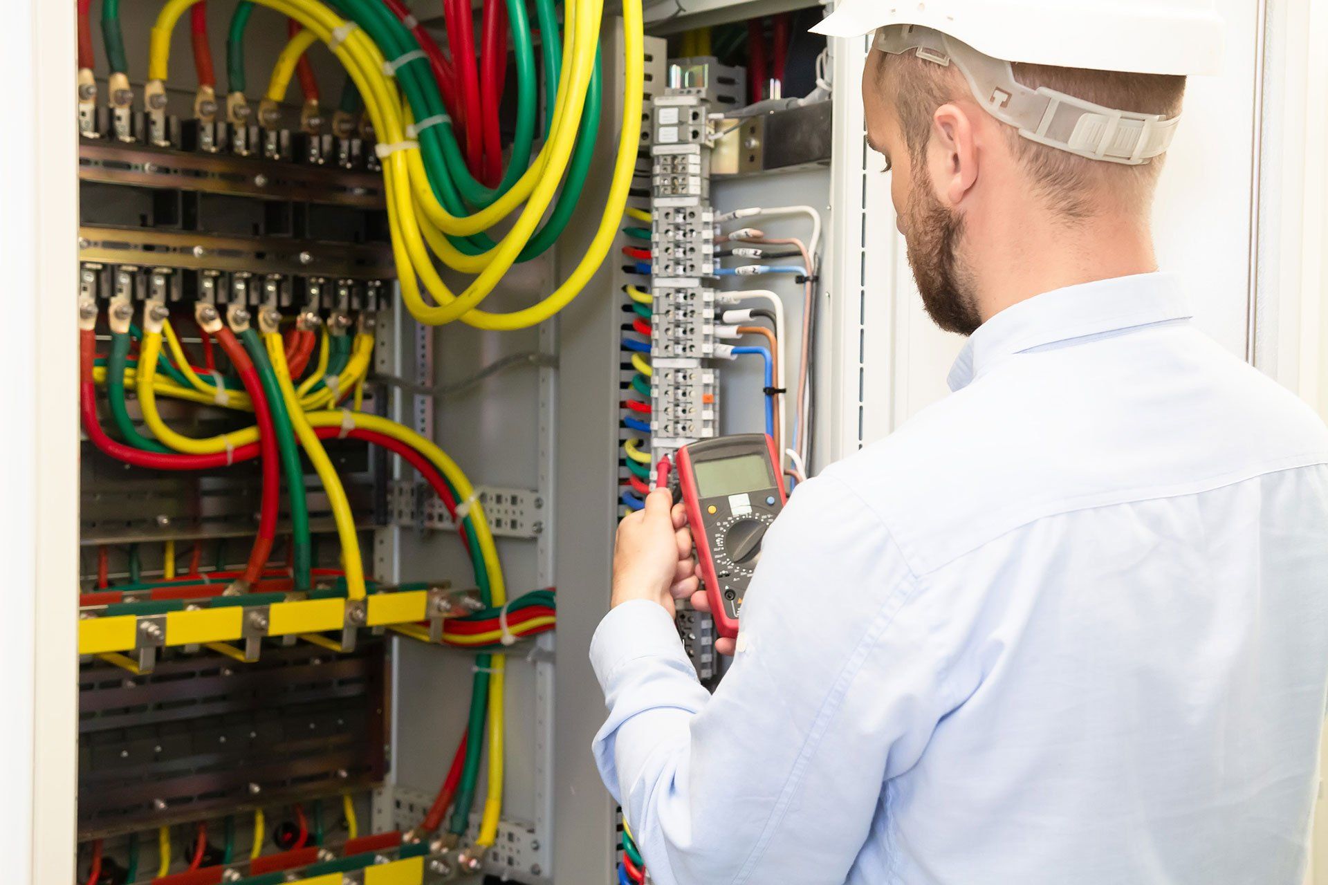Electrician engineer with measuring tool works in electrical cabinet