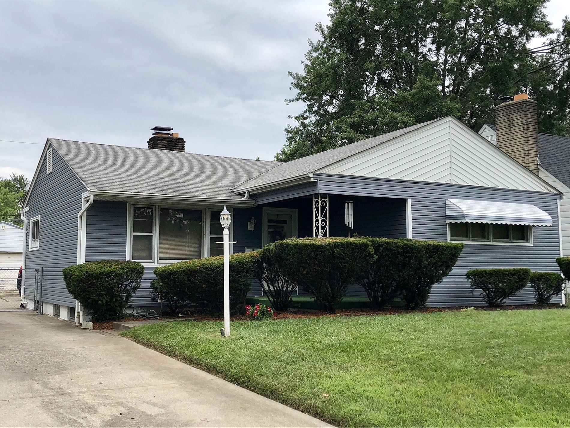 A blue house with a gray roof and a white awning is sitting on top of a lush green lawn.