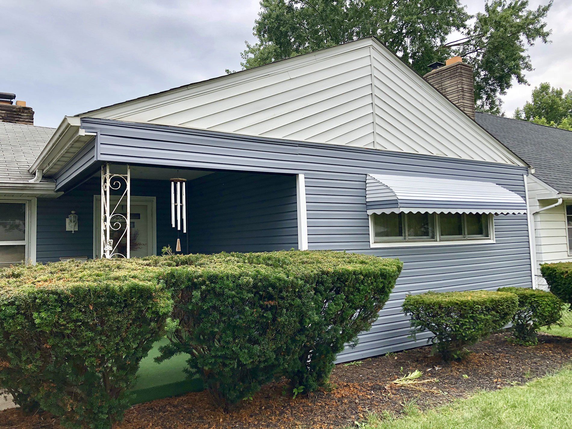 A house with a blue siding and a white awning on the front porch.