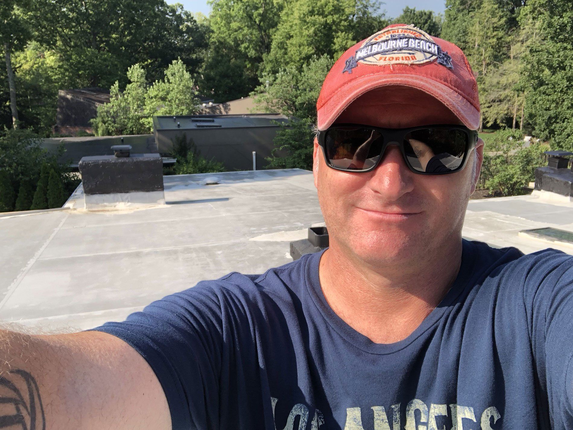 A man wearing sunglasses and a hat is taking a selfie on a roof.