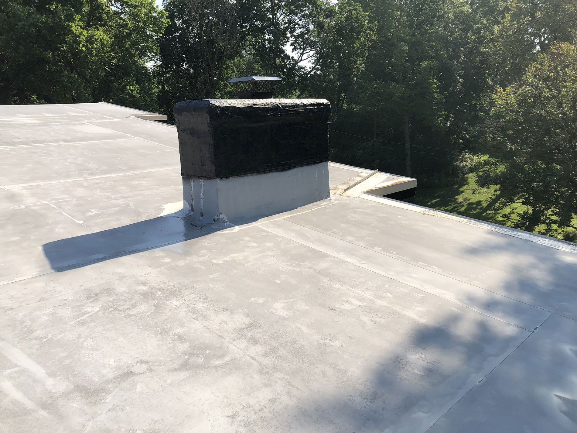 A roof with a chimney on it and trees in the background.