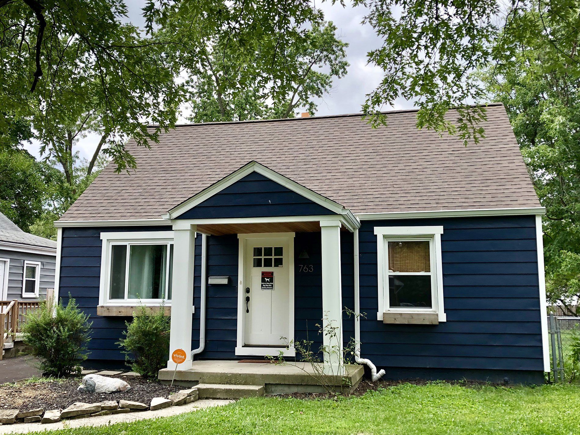 A blue house with a brown roof and white trim is sitting on top of a lush green lawn.