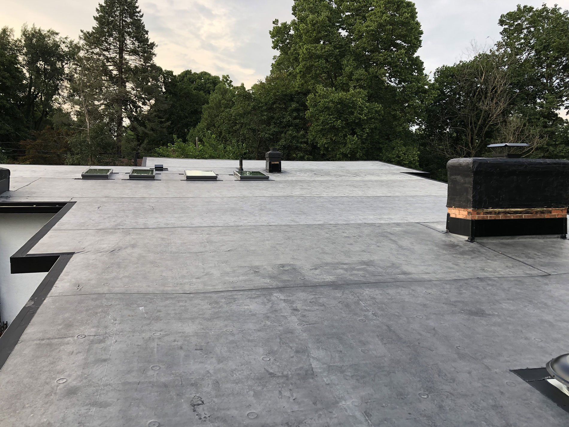 A roof with a chimney on it and trees in the background.