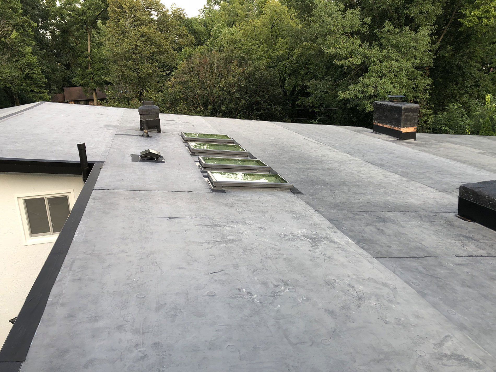 A roof with a chimney on it and trees in the background.