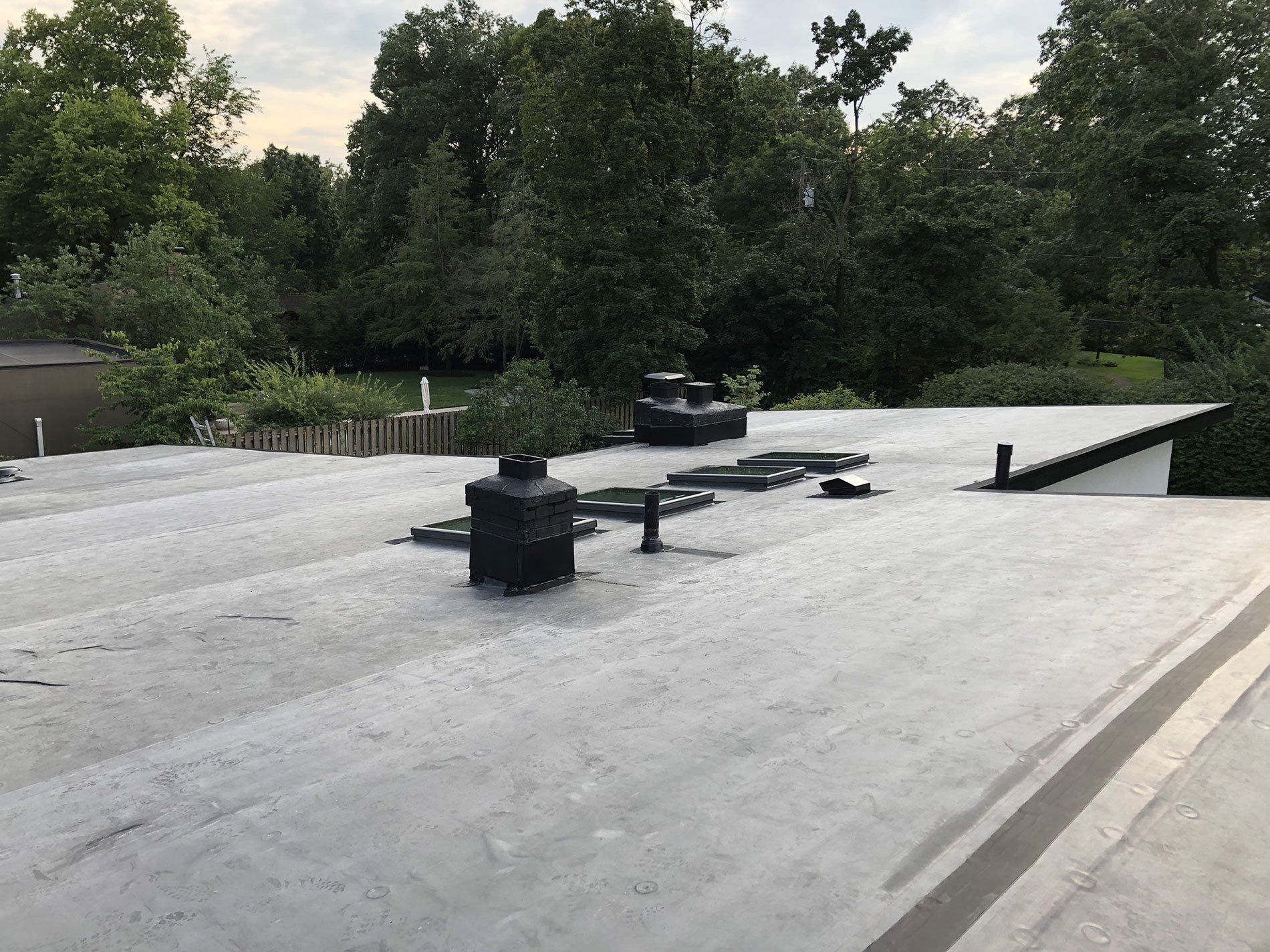 A roof with a chimney on it and trees in the background.