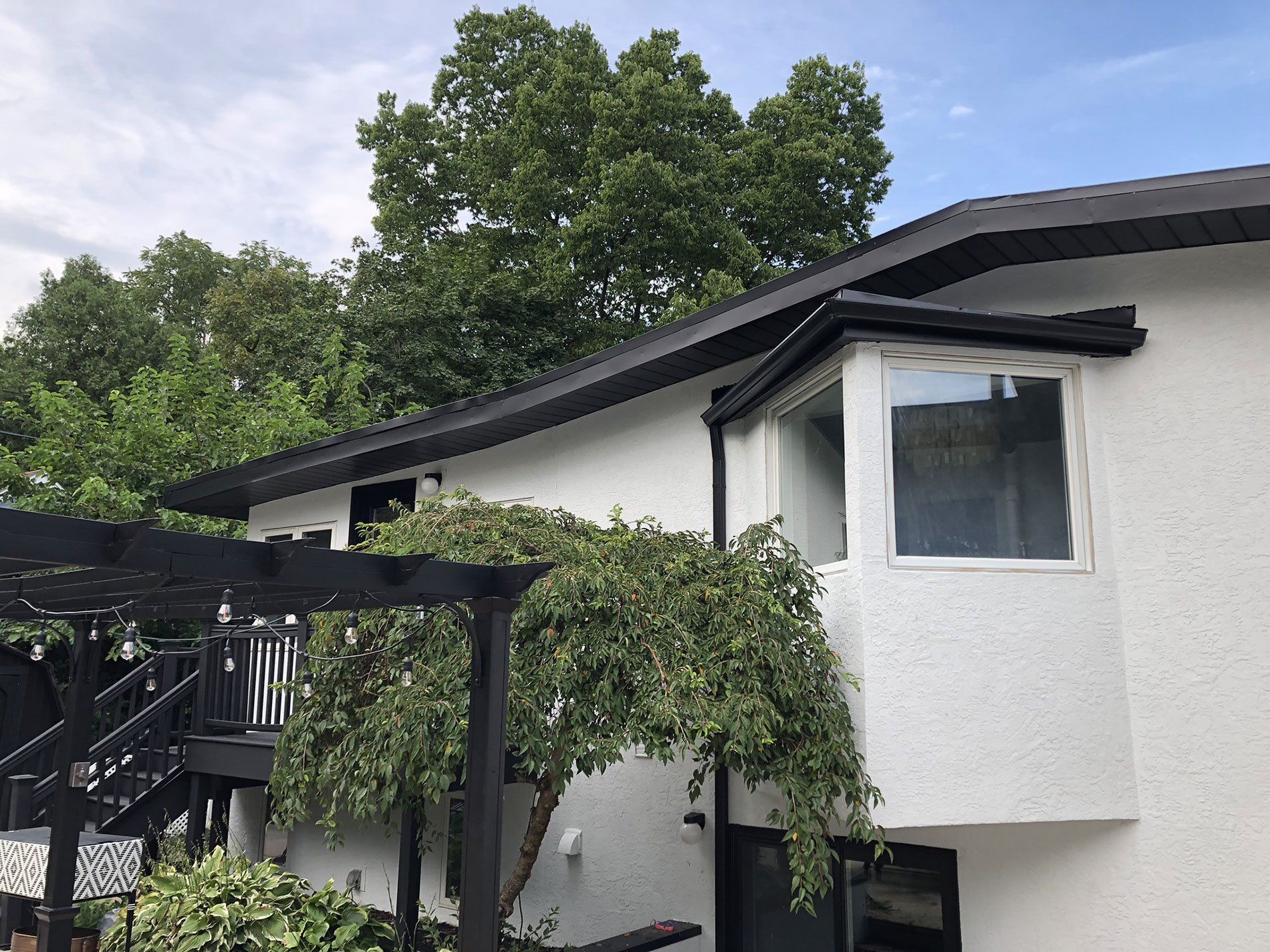 A white house with a black roof and a tree in front of it