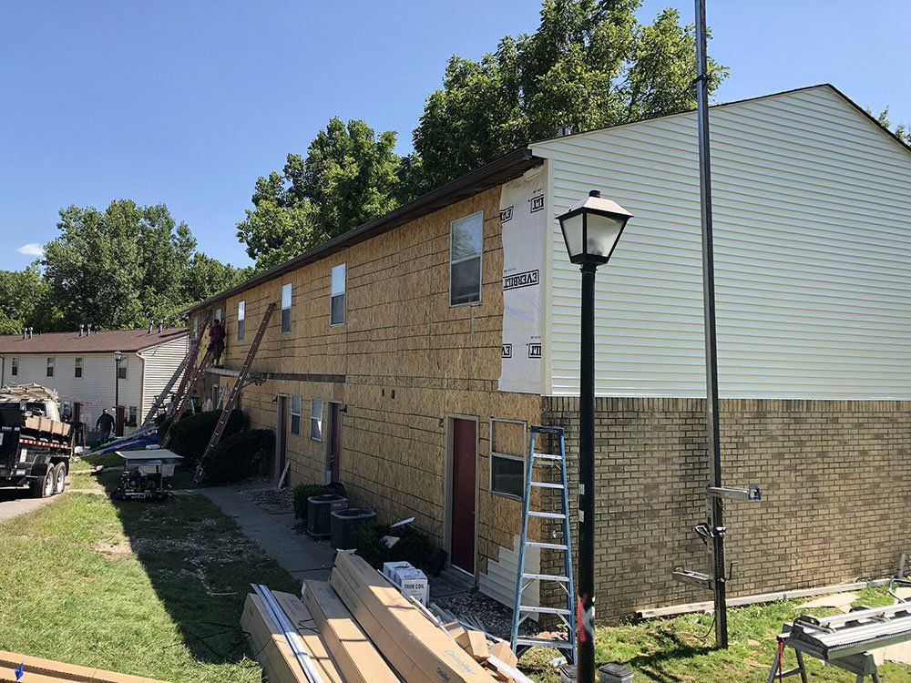 A brick building is being remodeled with siding and a lamp post.