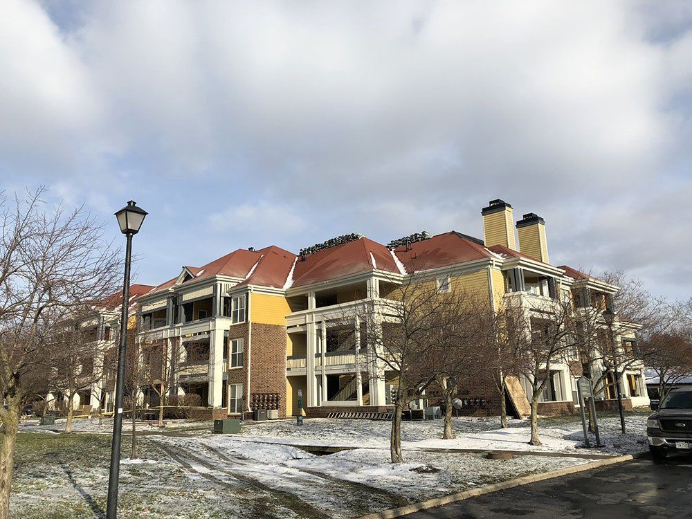 A large apartment building with a red roof is surrounded by snow and trees.