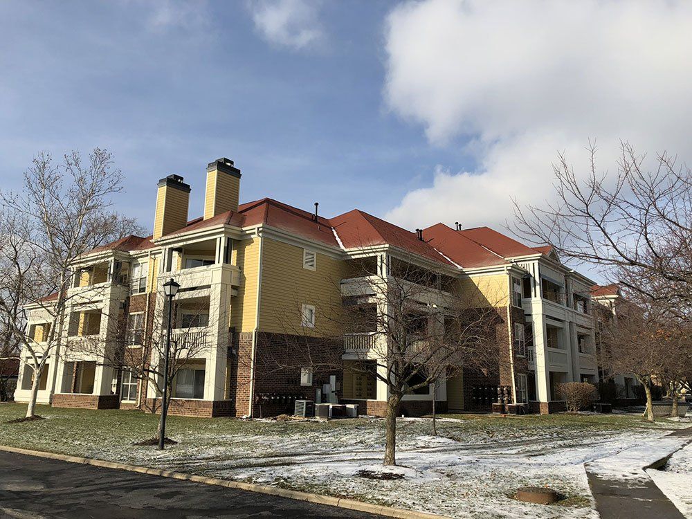 A large apartment building with a red roof is surrounded by snow and trees.