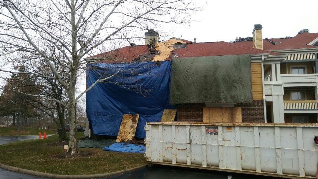 A dumpster is parked in front of a building with a blue tarp on it.