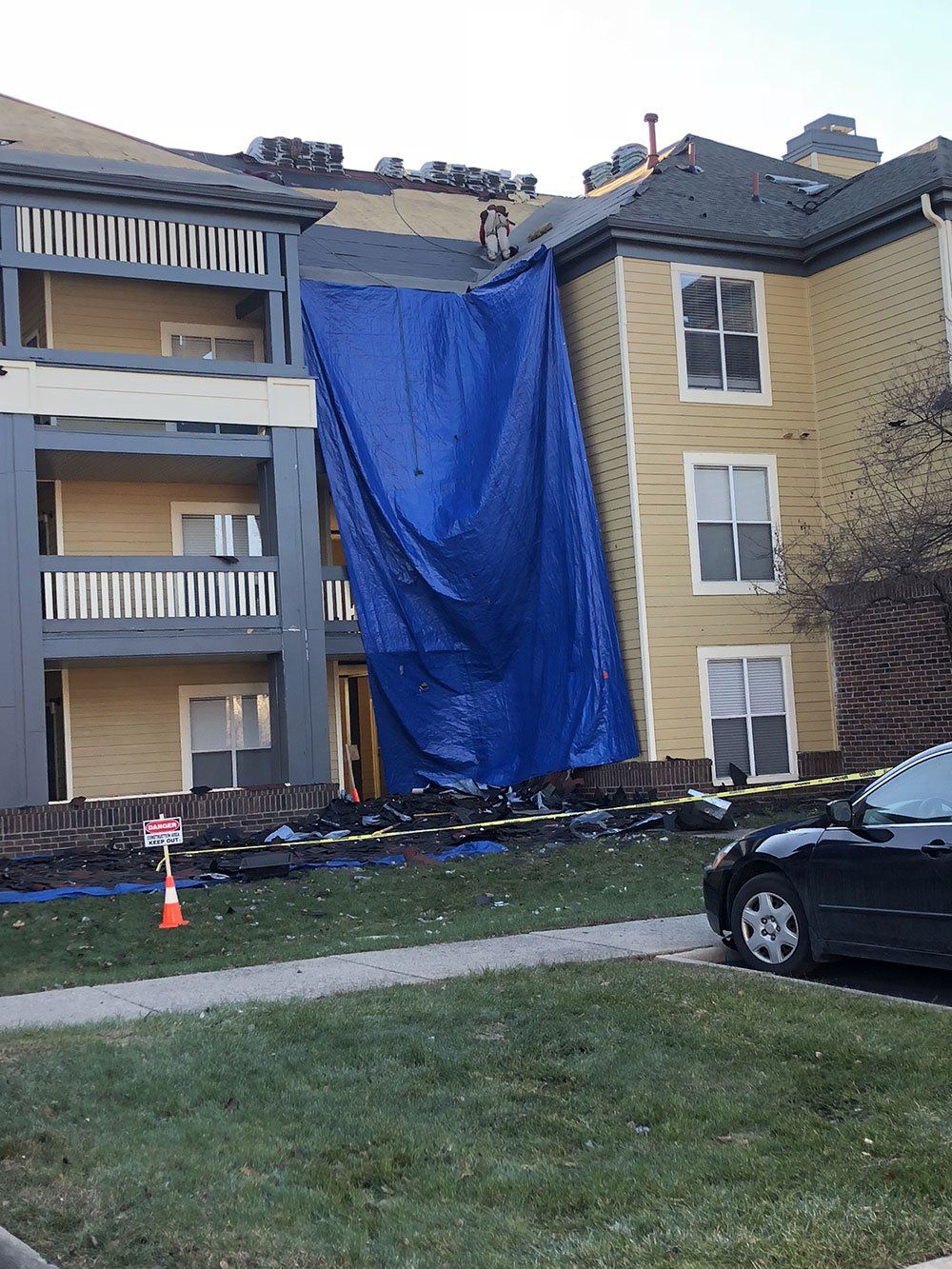 A building with a blue tarp on it and a car parked in front of it.