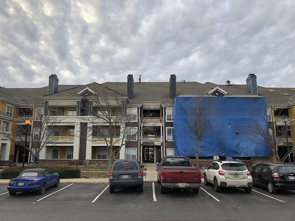A row of cars are parked in front of a large apartment building.