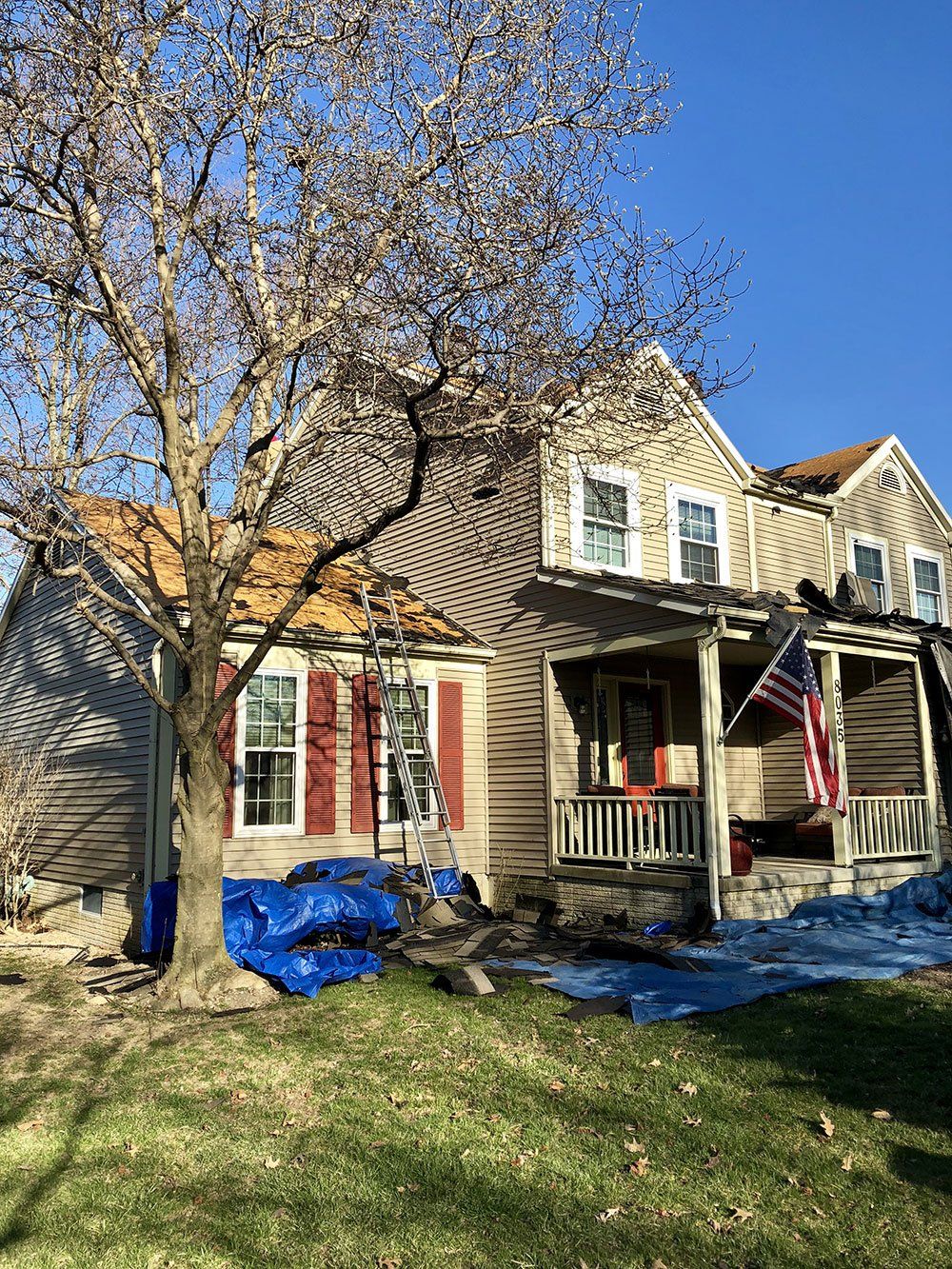 A large house with a porch and a tree in front of it.